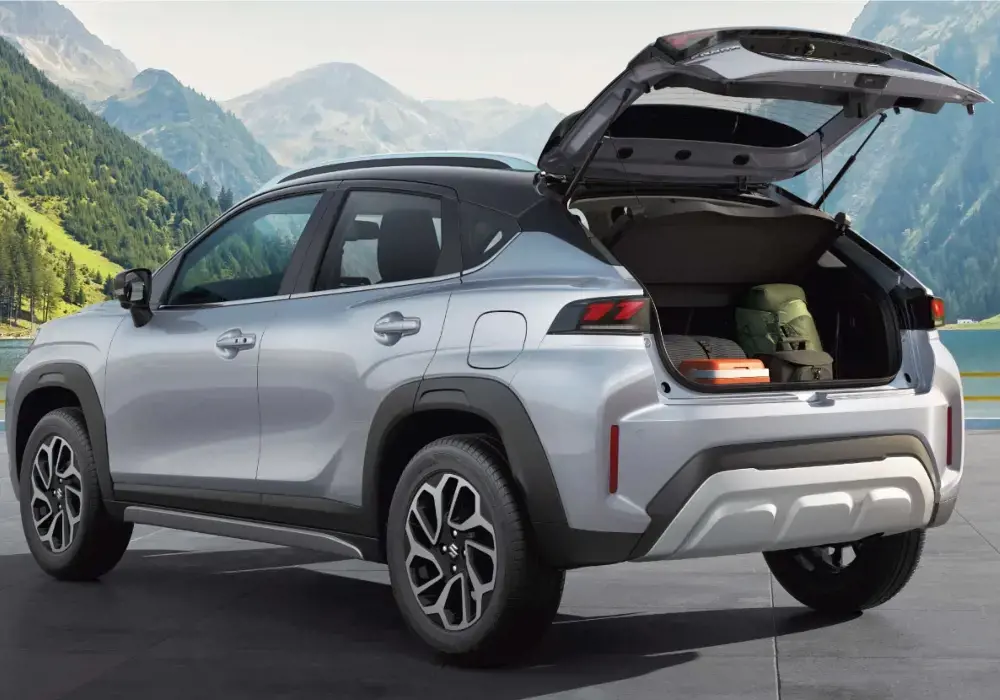 Vista trasera de un SUV Suzuki de color plateado, estacionado frente a un paisaje montañoso con un lago.