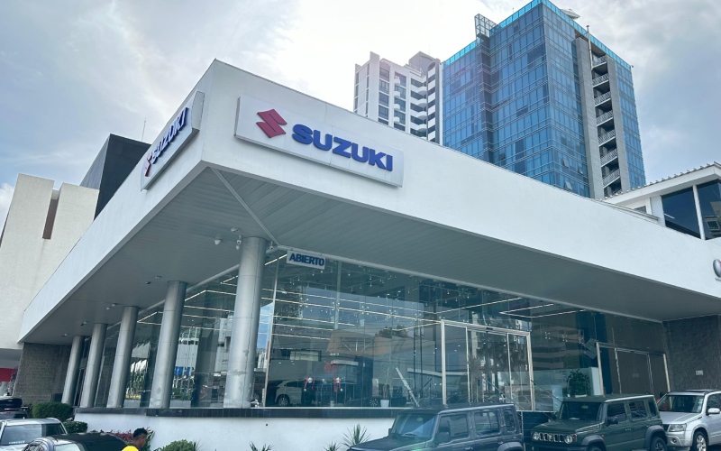 Edificio moderno con el logo de Suzuki en la entrada y varios vehículos de la marca expuestos en la parte delantera.